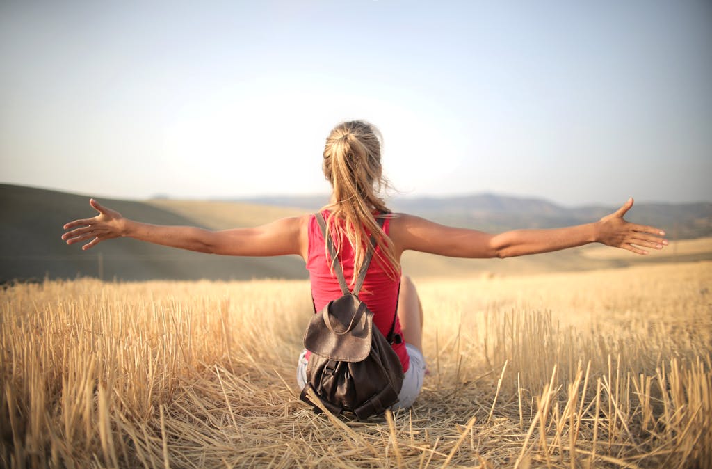 Woman enjoying the open air and freedom while sitting in a hay field during sunset.